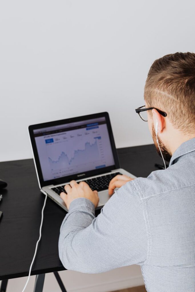 Maximizing ROI with Facebook, Google, YouTube, and Instagram Ads A man uses a laptop indoors to analyze stock market trends graph on screen.